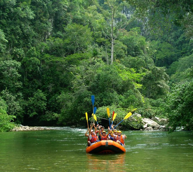 rafting-rio-claro-marble-canyon-medellin-day-trip Group of rafters raising colorful paddles on the Río Claro river surrounded by tropical rainforest and marble cliffs near Medellín, Colombia
