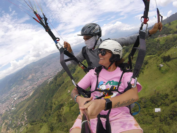 A smiling adventurer captures a GoPro selfie while paragliding with a certified pilot, showcasing a top day trip from Medellin.