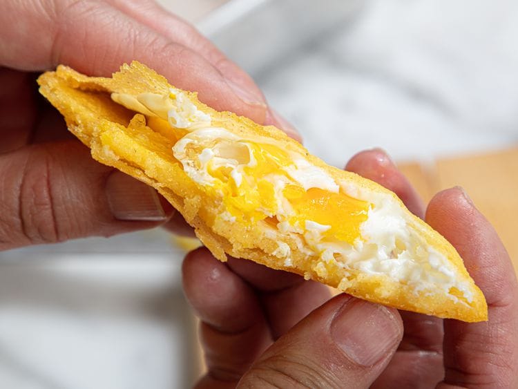 A close-up of a hand holding a freshly fried Arepa de Huevo, a classic Colombian breakfast food from the Caribbean coast.