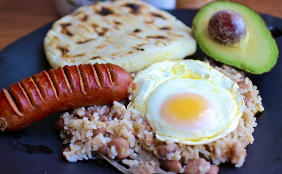 A close-up of Calentao, the quintessential breakfast Colombian style, featuring reheated rice and beans, a fried egg, chorizo, and an arepa.