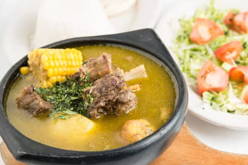 A comforting bowl of Sancocho, a traditional Colombian dish with beef, corn, and potatoes, which is flavorful but not spicy until you add ají.