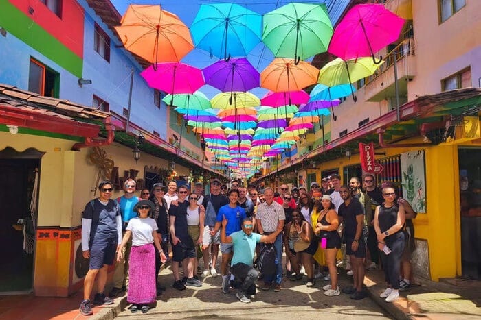 A happy tour group poses under the famous umbrella street in Guatapé, a colorful highlight of this day trip from Medellin, Colombia.