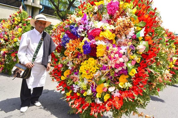 A silletero in traditional clothing stands beside his massive, colorful silleta, embodying the rich history of why the Festival of Flowers is celebrated in Medellín.