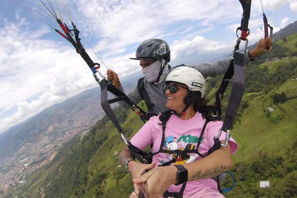 A smiling adventurer captures a GoPro selfie while paragliding with a certified pilot, showcasing a top day trip from Medellin.
