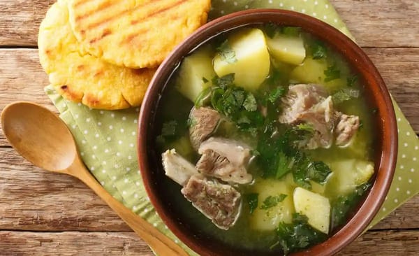 A steaming bowl of Caldo de Costilla, a hearty beef rib soup with potatoes and cilantro, a popular and revitalizing Colombian breakfast.