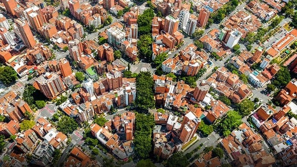 Aerial view of a dense, green urban area with red-tiled roofs, showing the intricate layout typical of a medellin neighborhoods.