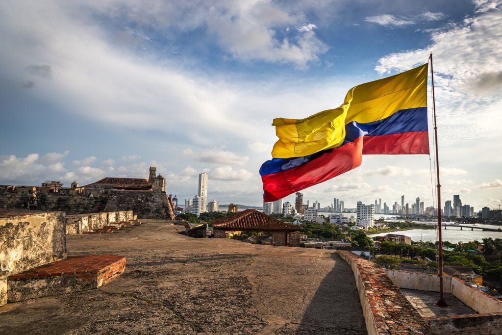 The Colombian flag waving over a historic city, setting the scene for a detailed guide about the cost of living in Colombia.