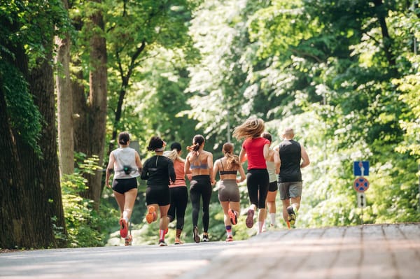A group of diverse runners from behind, moving away from the camera on a paved path surrounded by lush green trees, embodying the active spirit of nature day trips from Medellin.