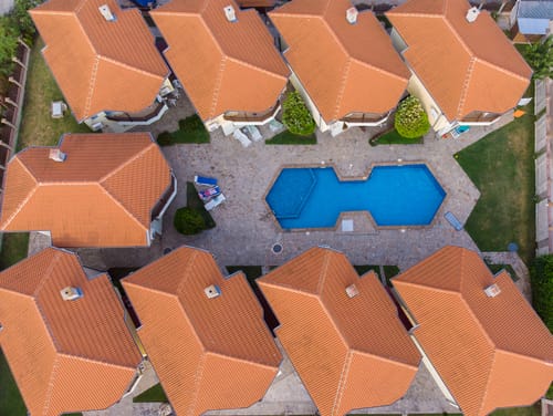 An aerial view of a residential complex with uniform terracotta-tiled roofs and a central swimming pool. This type of modern, planned development is often associated with new real estate investments driving gentrification in Medellin.