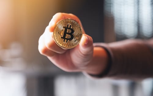 Hand holding a Bitcoin coin, illustrating the use of Bitcoin for payments and transactions in crypto Medellin.